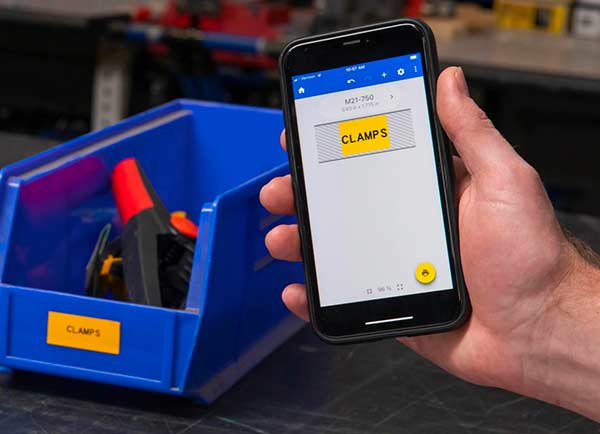 Et labeldesign på en Ekspreslabels-mobilskærm ved siden af den faktiske udskrevne label. Begge har en stærk gul farve og skriften “CLAMPS”.