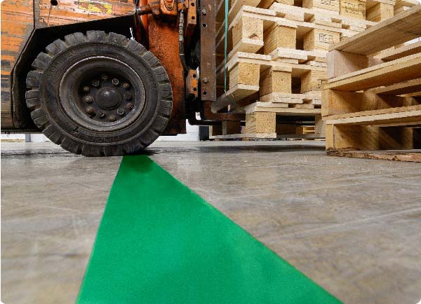 En stor gaffeltruck kører over en linje markeret med grøn ToughStripe Max-gulvtape. Kanterne af tapen er ubeskadigede af gaffeltruckens solide hjul.